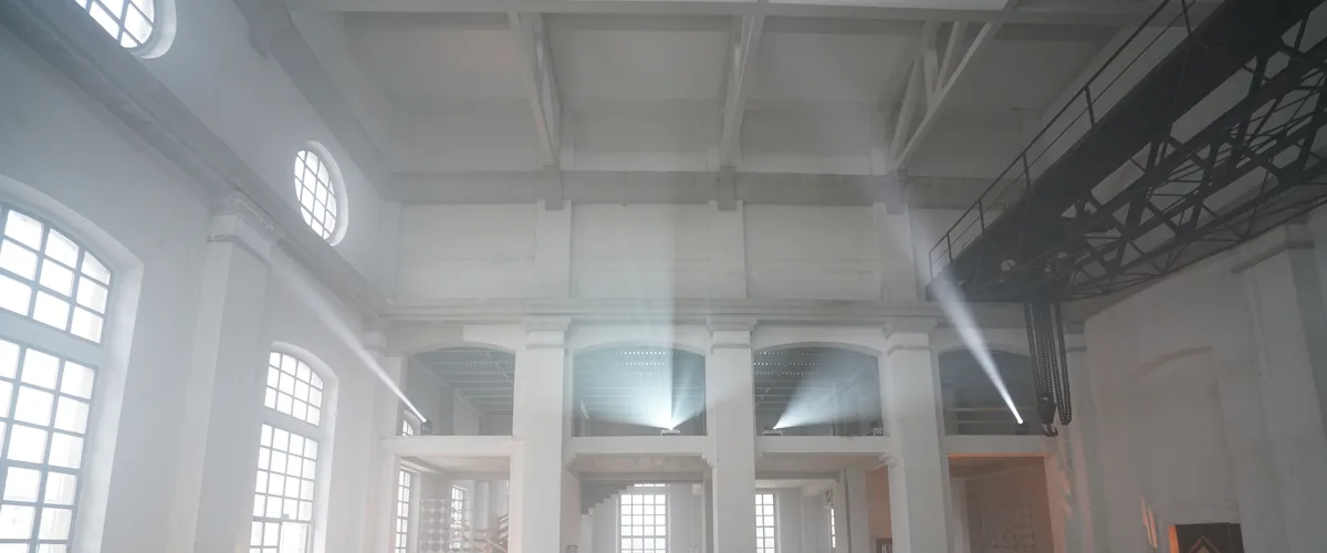 Interno della Ex Centrale ENEL di Bergamo — spazio industriale vuoto con fasci di luce, carroponte, finestre ad arco e oblò, prima dell'intervento SUONO E LUCE