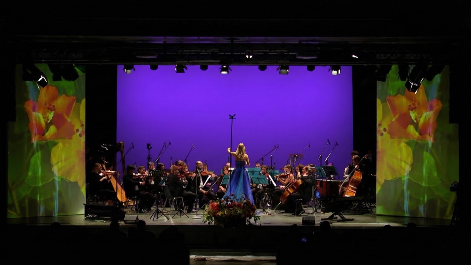 Orchestra Ars Armonica con videoproiezione di fiori arancio sulle quinte e fondale viola — scenografia digitale per il Concerto per la Natura, Sala Oggioni Bergamo 2022, SUONO E LUCE