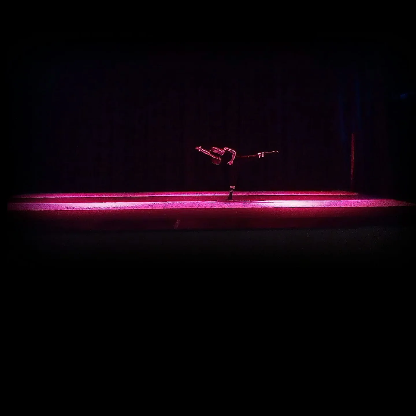 Solista in arabesque su palco illuminato da una lama di luce magenta nel buio — light design per la danza, SUONO E LUCE