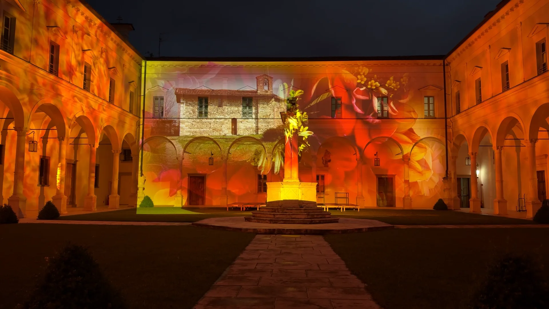 Chiesetta in pietra con fiori arancio proiettata sulla facciata del chiostro benedettino — videomapping architetturale e valorizzazione del territorio, Abbazia di San Paolo d'Argon, SUONO E LUCE