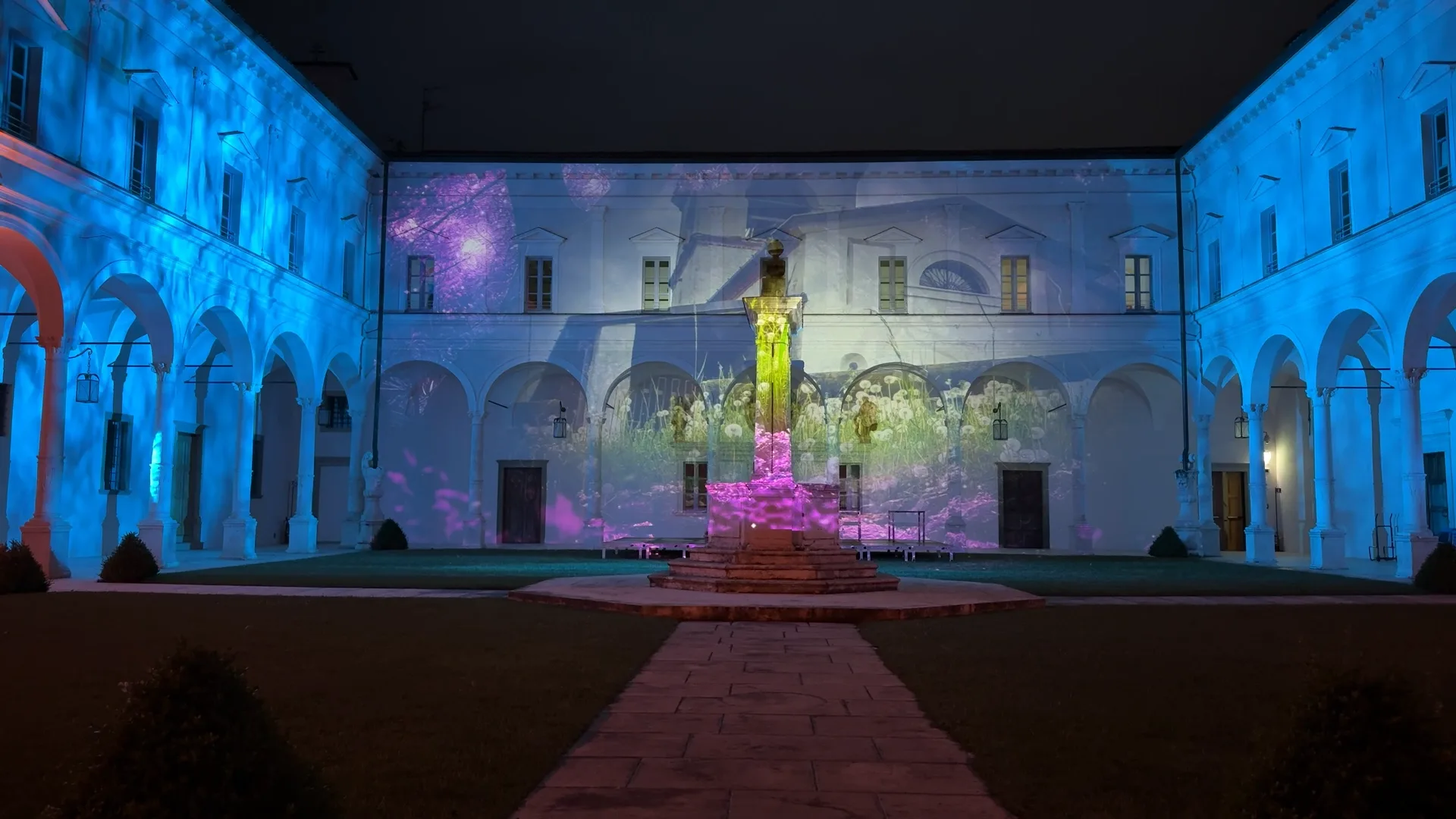 Fiori viola e gialli con chiesa del territorio proiettati sulla facciata del chiostro — spettacolo immersivo di videomapping e proiezioni architetturali, Abbazia di San Paolo d'Argon, SUONO E LUCE